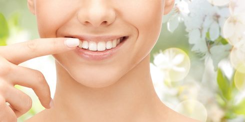 Frau zeigt auf weiße Zähne in ihrem Mund durch Kurkuma - Zahnpasta